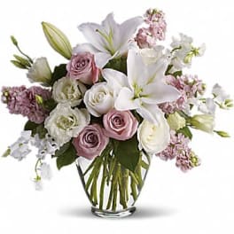 White lilies and pale pink and white roses arranged in a clear glass vase