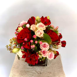 Compact arrangement of red and pink roses with red alstroemeria in a dark glass cube vase