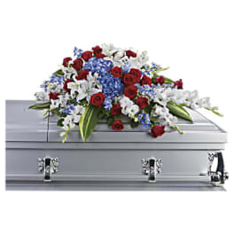 Red, white, and blue casket spray of roses, lilies, and hydrangea on a silver casket