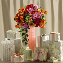 Tall pink vase arrangement of orange tulips, pink peonies, and roses surrounded by pastel gift boxes