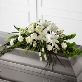 White floral casket spray with lilies, roses, and carnations on a gray casket