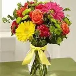 Mixed bouquet of bright flowers in a clear glass vase with a yellow ribbon