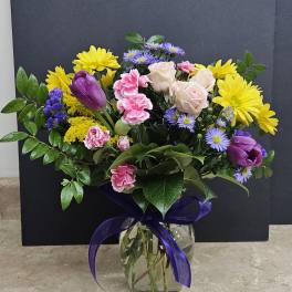 Mixed bouquet of yellow daisies, pink roses, and purple tulips in a glass vase