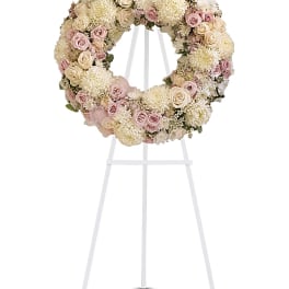 Circular floral wreath of pink and cream roses on a white stand