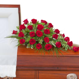 Red rose casket spray arranged on a closed wood casket with white interior