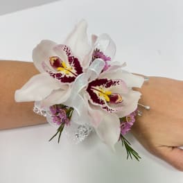 Wrist corsage with two white orchids, pink accents, and white ribbon on an arm