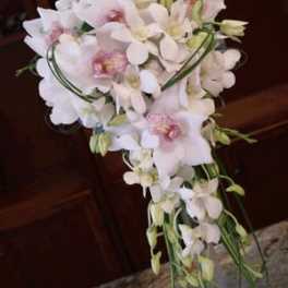Cascading bridal bouquet of white orchids with pink centers displayed in a clear glass vase