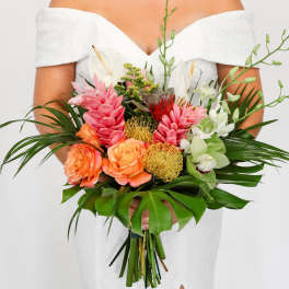Bride in an off-shoulder white dress holding a large tropical bouquet of pink, orange, green, and white flowers.