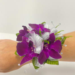 Purple orchid wrist corsage with white ribbon and beads worn on an arm