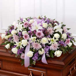 Lavender and white casket spray of roses, lilies, and mums with ribbon on a wooden casket