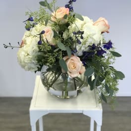 Bouquet of pale roses, white hydrangeas, and blue flowers in a glass vase