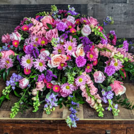 Low spray of pink and purple roses, mums, and snapdragons arranged in a wide mound.