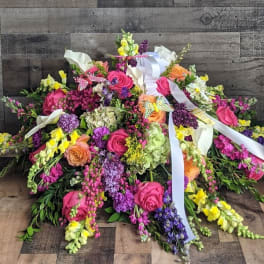 Bright mixed casket spray with pink roses, yellow snapdragons, hydrangeas, and white ribbons.