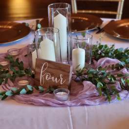 Table centerpiece with candles, greenery, and a wooden sign
