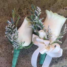 Two small white rose boutonnieres with greenery and ribbon