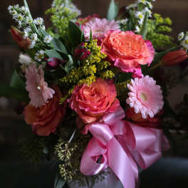 Pink and coral roses with daisies in a white vase, tied with a pink ribbon