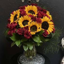 Bouquet of red roses and yellow sunflowers in a clear glass vase