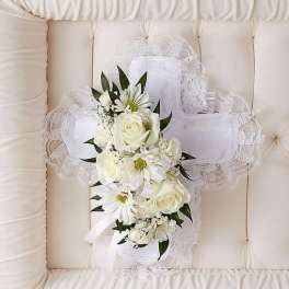 White floral cross pillow with roses and daisies resting on a cream tufted casket interior.