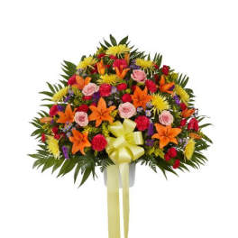 Fan-shaped arrangement of orange lilies, pink roses, red carnations and yellow mums in a white container with yellow bow
