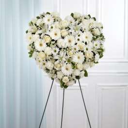 Heart-shaped standing spray of white roses, lilies, and mums on a tall metal easel