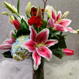 Bouquet of pink lilies, hydrangea, and red carnations in a glass vase