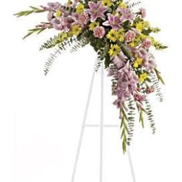 Standing spray of pink lilies, pink carnations, and yellow daisies on a white easel.