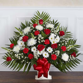 Fan-shaped red and white floral arrangement with roses and daisies in a white container with red bow