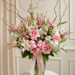 Tall pink and white arrangement with roses and lilies in a clear vase with a pink bow