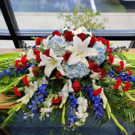 Large floral casket spray with white lilies, red roses, and blue hydrangeas