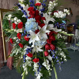 Large standing floral spray with red roses, white lilies, and blue flowers