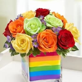 Rainbow rose bouquet in a clear cube vase with striped wrap