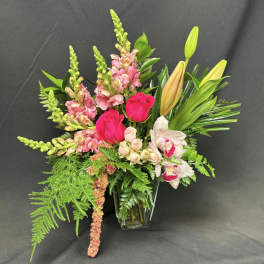 Pink roses and orchids in a clear glass vase with tall greenery