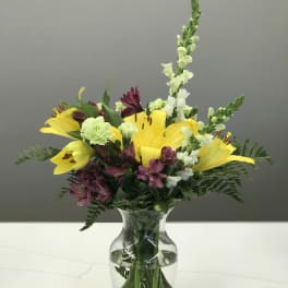 Yellow lilies and purple flowers arranged in a clear glass vase