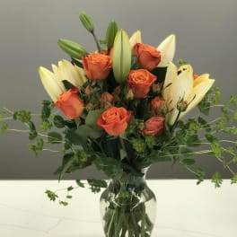 Orange roses and cream lilies in a glass vase