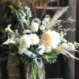 White floral arrangement in a clear glass vase with calla lilies and dahlias