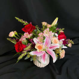 Mixed bouquet with pink lilies, red and peach roses in a white vase