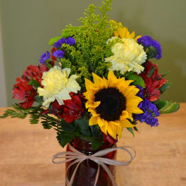 Mixed bouquet in a red glass vase with a sunflower and carnations