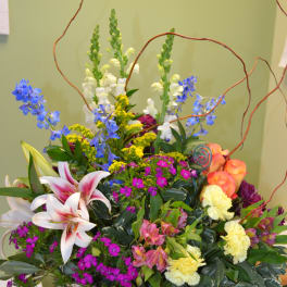 Colorful mixed flower arrangement in a white basket with tall curly branches