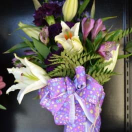 Bouquet of lilies and purple flowers in a lavender vase with a ribbon