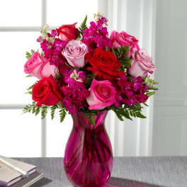Pink and red roses arranged in a magenta glass vase