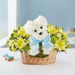White teddy bear in a wicker basket surrounded by yellow flowers