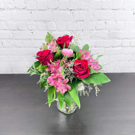 Pink roses and alstroemeria in a clear glass vase with a pink heart pick