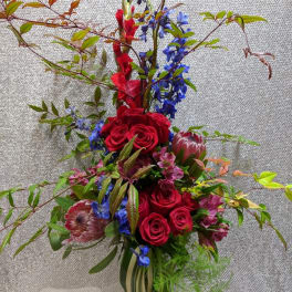 Tall bouquet of red roses, blue flowers, and protea in a glass vase