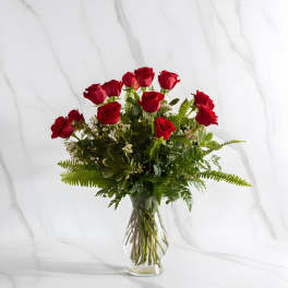 Red roses arranged in a clear glass vase with greenery