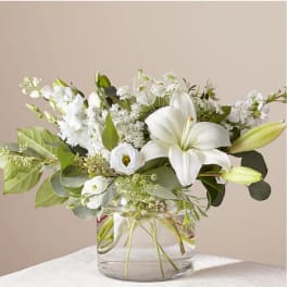 White lilies and small white flowers in a clear glass vase