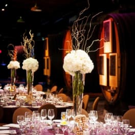 Tall white floral centerpieces on banquet tables in a dim event hall