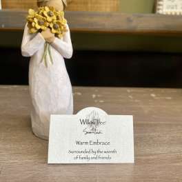 Small figurine holding a bouquet of yellow flowers with a name card