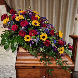 Casket spray with red roses, sunflowers, and purple flowers