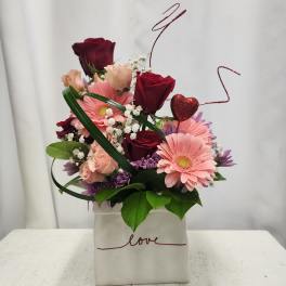 Pink and burgundy flower arrangement in a white box with a heart pick