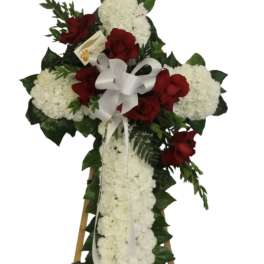 Standing white floral cross with red roses and white bow on an easel